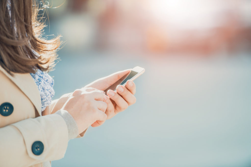 Young woman walking and using a smart phone on a city street.