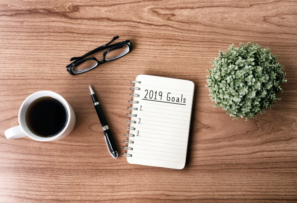 2019 goals text on notepad with a pen, glasses and a coffee cup next to it