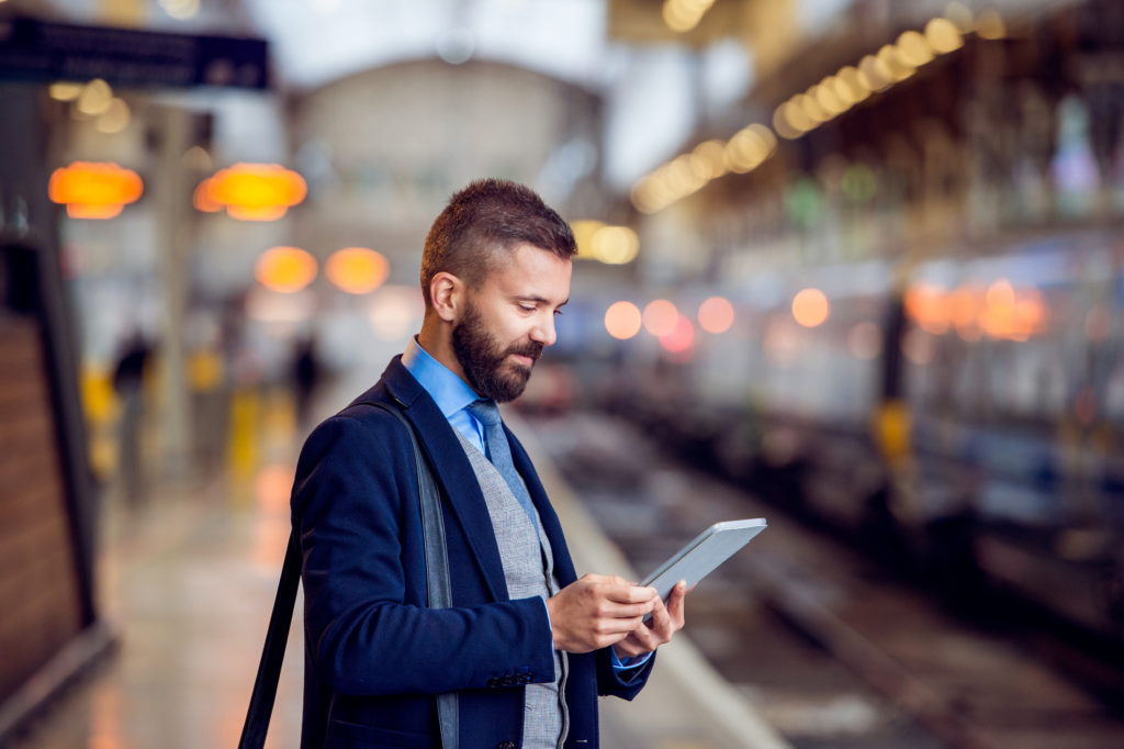 businessman holding a tablet, waiting on a train platform