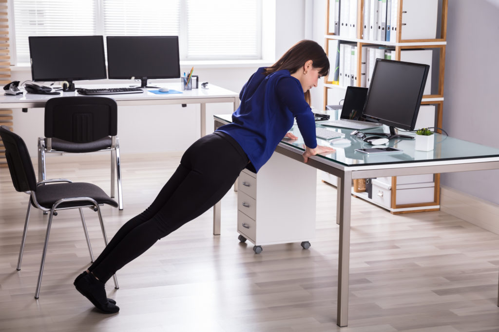 Side View Of A Young Businesswoman Doing Push Up On Office Desk