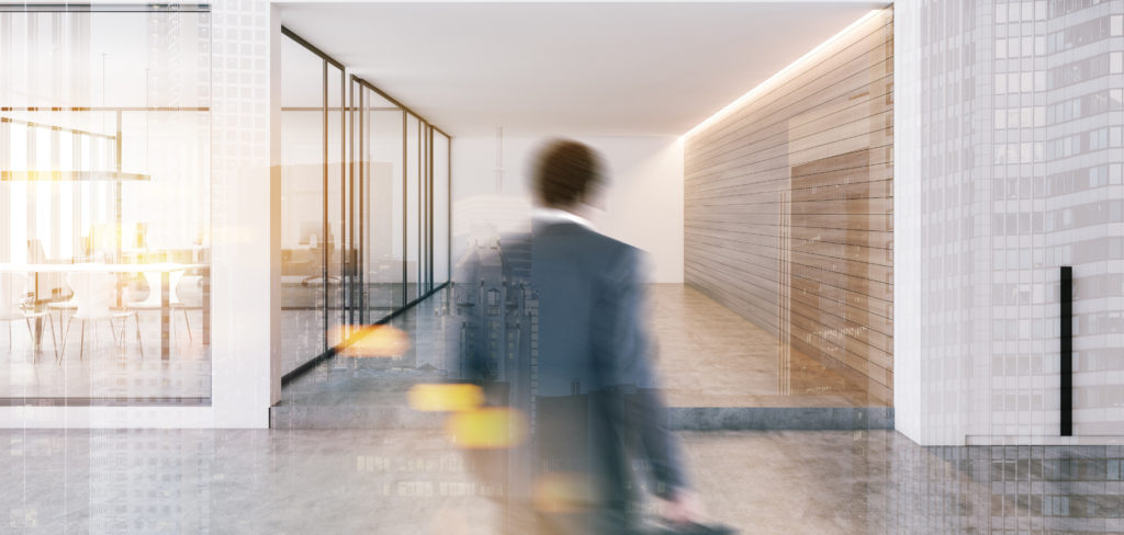 Businessman entering modern office with white and wooden walls, concrete floor and conference room with glass doors.